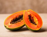 Juicy papaya cut in half showing dark seeds, on a neutral textured background.