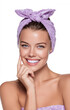 © Irina - Portrait of beautiful young smiling woman with lilac headband wrapped in white towel. Woman holds hands near face on white background. Concept of facial care, spa treatments