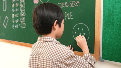 Poster - Asian boy drawing picture to express and develop imagination while standing at blackboard in classroom. Attractive elementary student writing at blackboard in art lesson. Education concept. Pedagogy.