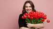 © Madihabibi - Smiling woman in black top holding a large bouquet of red tulips against a pink background portrait