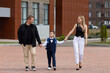 © Irina Mikhailichenko - Little son schoolboy with backpack holding hands of father and mother, going to first grade on autumn day. Parents and little child on the way to school. Happy family and children education concept
