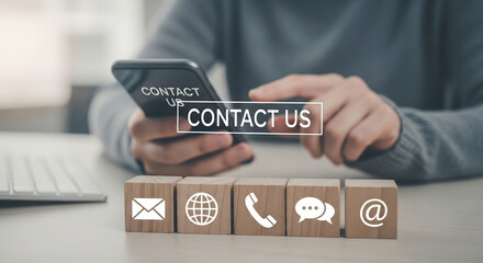 Poster - Person using phone with contact us message above wooden blocks with contact icons on the table top