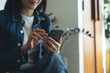 © tippapatt - Woman using mobile phone at coffee shop. Smiling asian freelancer, entrepreneur in blue jeans using smartphone, surfing the internet at cafe