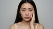 © Imagine Stuff - Portrait of a Young Asian Woman Touching Her Face with Concern