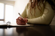 © Соня Монштейн - Woman working writing in notebook at home desk in daylight, taking notes in notepad sitting at table, brainstorming, journaling or business planning, focus on female hand holding pen
