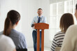© New Africa - Man giving public speech at lectern in front of audience indoors
