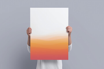 Poster - Individual holding a large blank poster with a gradient design transitioning from soft orange to light peach, showcasing a creative mockup for design purposes and copy space availability