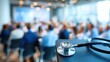 © JT Studio - A stethoscope rests on a table in the foreground as a medical seminar with attendees takes place in a bright, modern conference room.