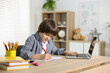 © New Africa - Cute little boy doing homework with laptop at table indoors