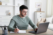 © New Africa - Man taking notes during online lesson at desk indoors. Self-study