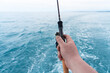 © Aleksei - Hand of a fisherman with a spinning rod with the line on a motor boat in the sea. Fishing rod and hands of fisherman over ocean water surface.