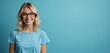 © Maryna - Attractive blond woman in blue t-shirt wears glasses. Smiling female model against blue background. Young, happy, stylish, confident person. Ophthalmologist, vision concept, eye care.