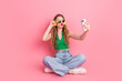 © deagreez - Young woman taking a selfie while sitting on a pink background, wearing modern casual clothes and sunglass