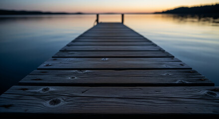Poster - Close-up view of dark wooden planks on a dock extending into calm water at sunset, showcasing serenity and tranquility