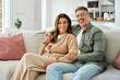 © insta_photos - Family portrait of happy middle aged mature romantic couple in their 50s hugging sitting on couch at home. Smiling older man and woman in love relaxing on sofa together in house living room.