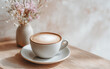 © Korkiat - A cup of coffee with milk and flowers in a vase on a beige table against a grey wall background, with copy space for text or design.