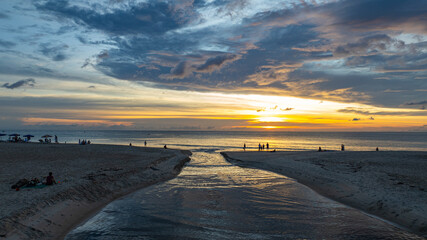 Wall Mural - the water from the canal flows to meet with the sea water. golden sparkles in the sky shine in the w