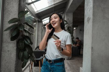Poster - Happy asian woman holding credit card and using smartphone for online shopping