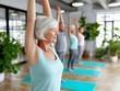 © Anzt Motion - Focused senior woman with short white hair and raised arms practicing a yoga pose during a group fitness class.