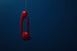 © Tithi - A vibrant red telephone handset suspended with a coiled cord against a deep blue background providing copy space