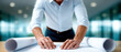 © javu - Man working on architectural blueprint with rolled plans on table in modern office