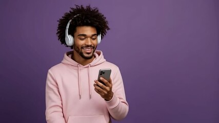 A smiling man listens to music on headphones while looking at his phone