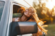 © SHOTPRIME STUDIO - Young woman with flowing hair smiles joyfully from a car window during sunset, showcasing freedom and adventure.