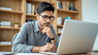 © Ada - Young serious indian professional business man, focused ethnic male student wearing glasses working on laptop, remote studying using computer looking at screen watching seminar webinar