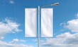 © artwiyanastudio - Two blank white vertical banners hang from a streetlight pole against a partly cloudy blue sky