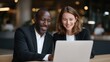 © si9nzation - Two Diverse Professionals Laughing Together Over a Laptop Screen in a Modern Office Sharing a Lighthearted Moment of Success and Collaboration at Work