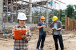 © skarie - Asian female engineer writing on clipboard while two male workers review plans on digital devices at a construction site. Teamwork and supervision in civil engineering project.