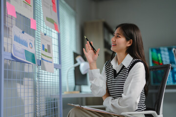 Poster - Asian businesswoman working with documents and financial chart at the office, using pen pointing at data hanging on a metal grid