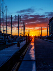 Wall Mural - A sun rise over a marina with silhouettes of masts of many boats and yachts docked. Teal and orange color scheme. Calm and relaxing mood. Port of Galway, Ireland.