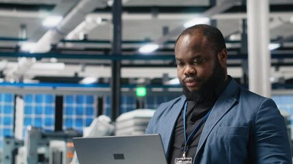 Poster - black solar energy specialist in a facility reviews data on laptop, inspecting manufacturing plant p