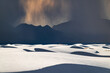 © Andrew Kornylak - White rolling sand dunes and dark mountains in the distance under a rain cloud at White Sands National Park, New Mexico. A group of hikers can be seen in the distance.
