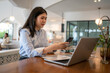 © Apichat - woman is sitting at a table with a laptop and a cell phone