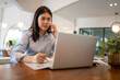 © Apichat - woman is talking on her cell phone while writing on a laptop