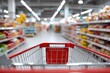 © The Little Hut - Wide-angle shot of an empty grocery store aisle with a red shopping cart in foreground showing shelves filled with colorful products and bright overhead lighting