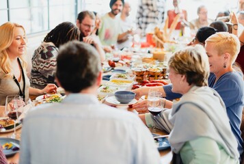 Poster - A diverse group of people enjoying a lively dinner party. Men and women of various ethnicities share laughter and delicious food at a long table filled with vibrant dishes.