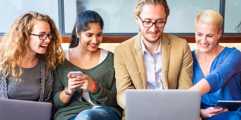 Poster - Group of four people collaborating, using laptops and phones. Diverse team working together, sharing ideas, and enjoying teamwork in a casual setting. Startup business team working on laptops.