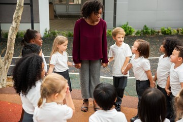 Poster - Teacher with diverse group of children outdoors. Kids in white uniforms. Engaged teacher, attentive children, diverse group, outdoor learning. Teacher at playground with elementary school kids.