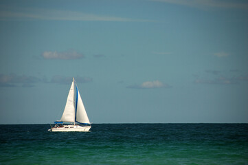  A white sailboat with blue accents sails peacefully on the turquoise ocean under a partly cloudy sky, creating a serene seascape