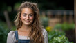 © Undersea - Young Caucasian woman with long wavy brown hair and natural makeup wearing denim overalls and light top smiling at camera in garden setting with soft bokeh background.