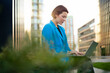 © Westend61 - Businesswoman working on laptop sitting by plants