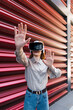 © Westend61 - Woman wearing virtual reality simulator and gesturing near corrugated iron