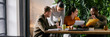 © Seventyfour - Website header shot of of diverse group of young adult and middle aged colleagues collaborating at table, reviewing documents and discussing business strategy in modern office with green plant wall