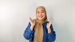 © Bimo Putra Dianata - Asian Muslim woman wearing hijab and blue dress looks surprised while raising both hands and closing her eyes, isolated on plain white background. Happy concept of getting good news.