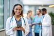 © benjamin - A smiling doctor holds a phone in a hospital setting. A warm and inviting image capturing a healthcare professional