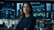 © Yuliia - Confident businesswoman in navy blue attire standing with crossed arms against background of digital trading screens and financial data displays in modern office.