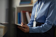 © DragonImages - Middle aged Caucasian woman sitting and writing on clipboard, wearing identification badge, partially visible in office environment, focusing on documenting information during prisoned context